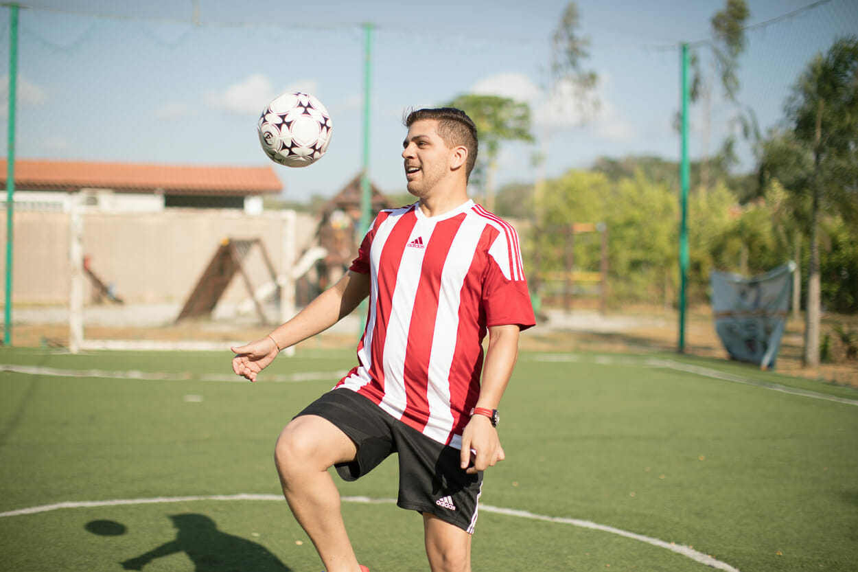 Hombre joven en uniforme de fútbol usando la rodilla para golpear la pelota en el estadio.