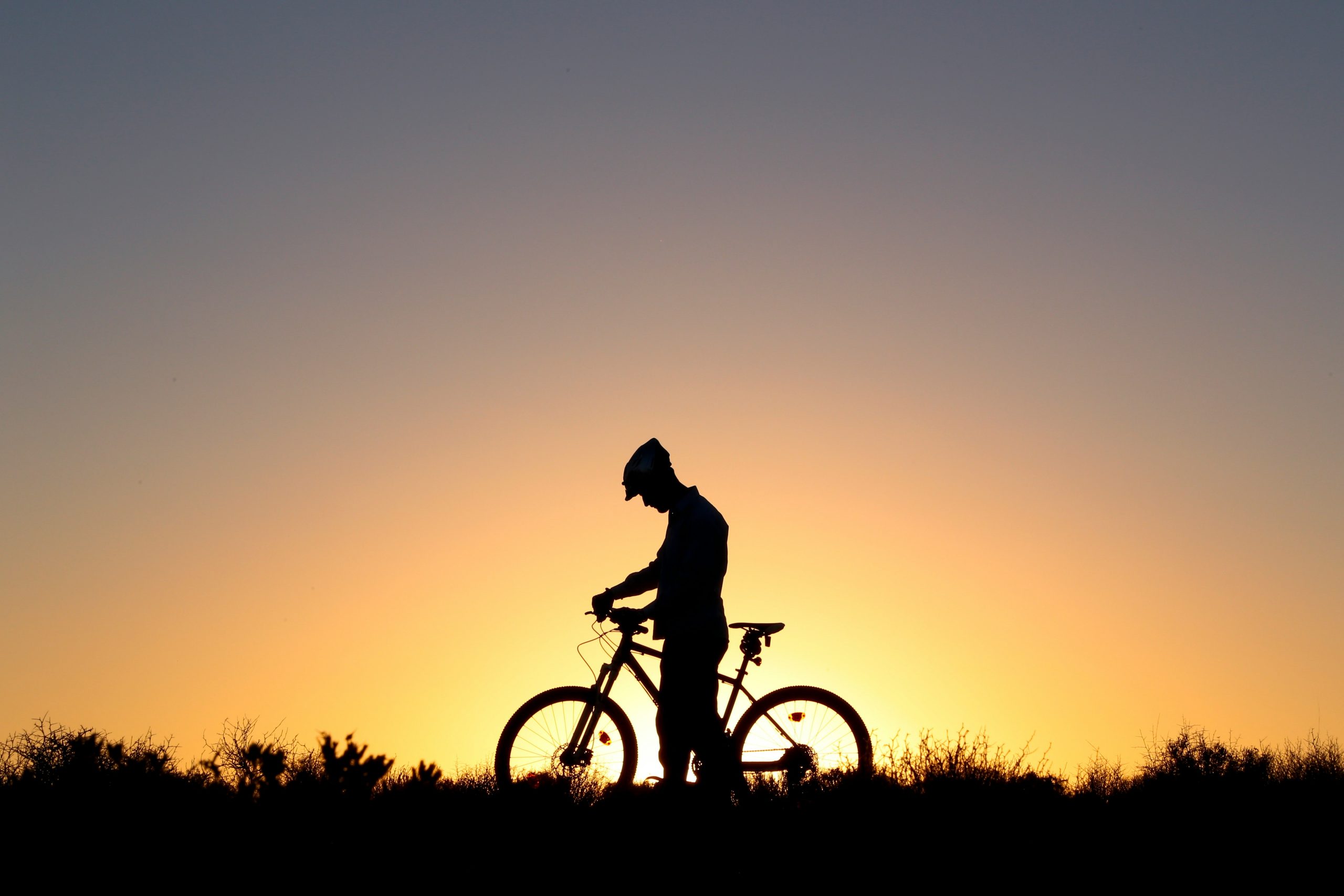 Ciclista con su bicicleta frente a un atardecer soleado.