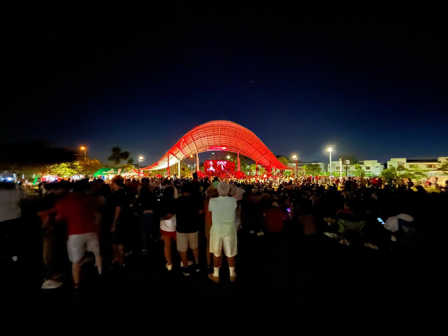 Personas observando un evento musical nocturno en la tarima techada del Parque RACH en Paseo del Norte.