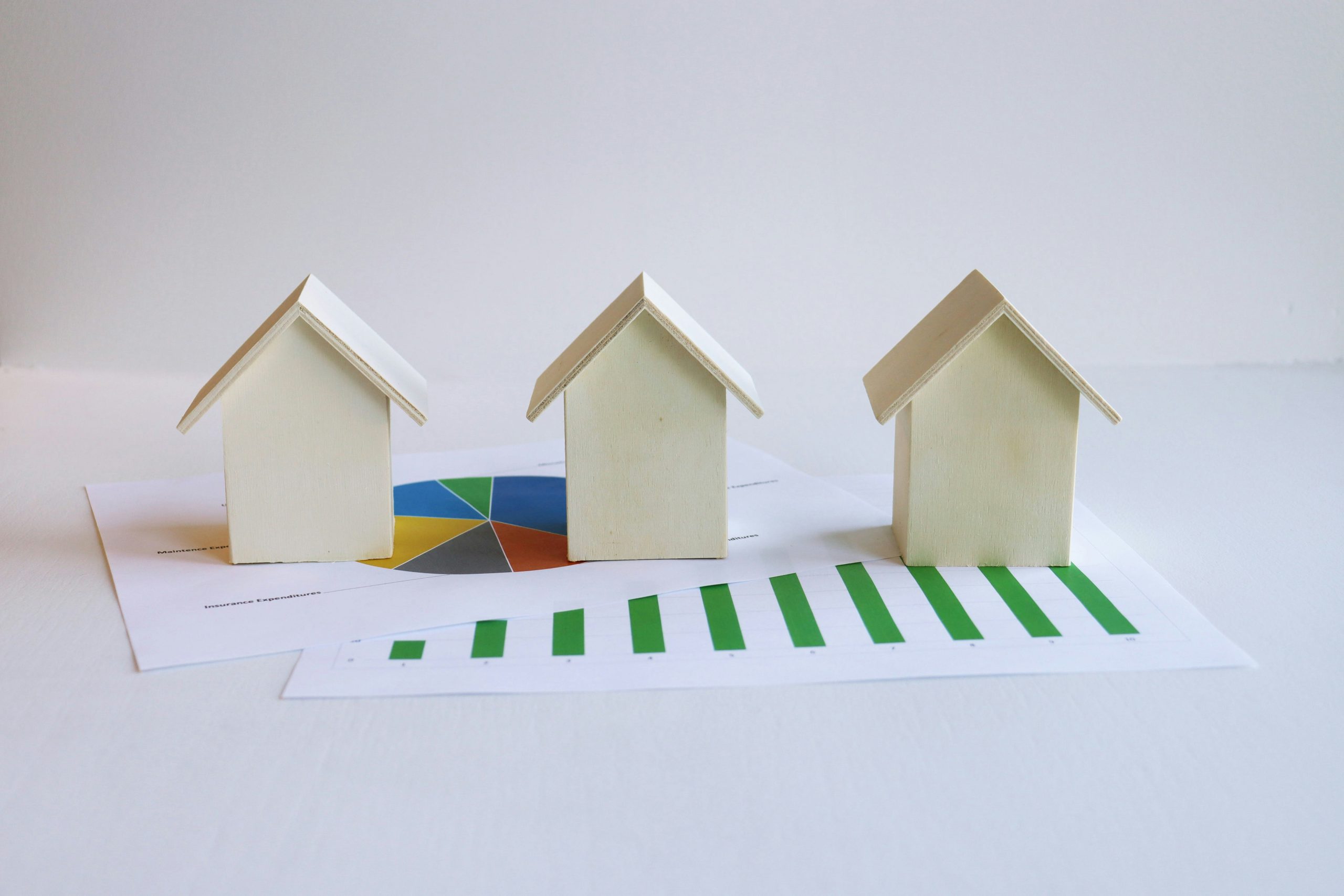 Tres maquetas en miniatura de casas sobre documentos con cálculos hipotecarios.