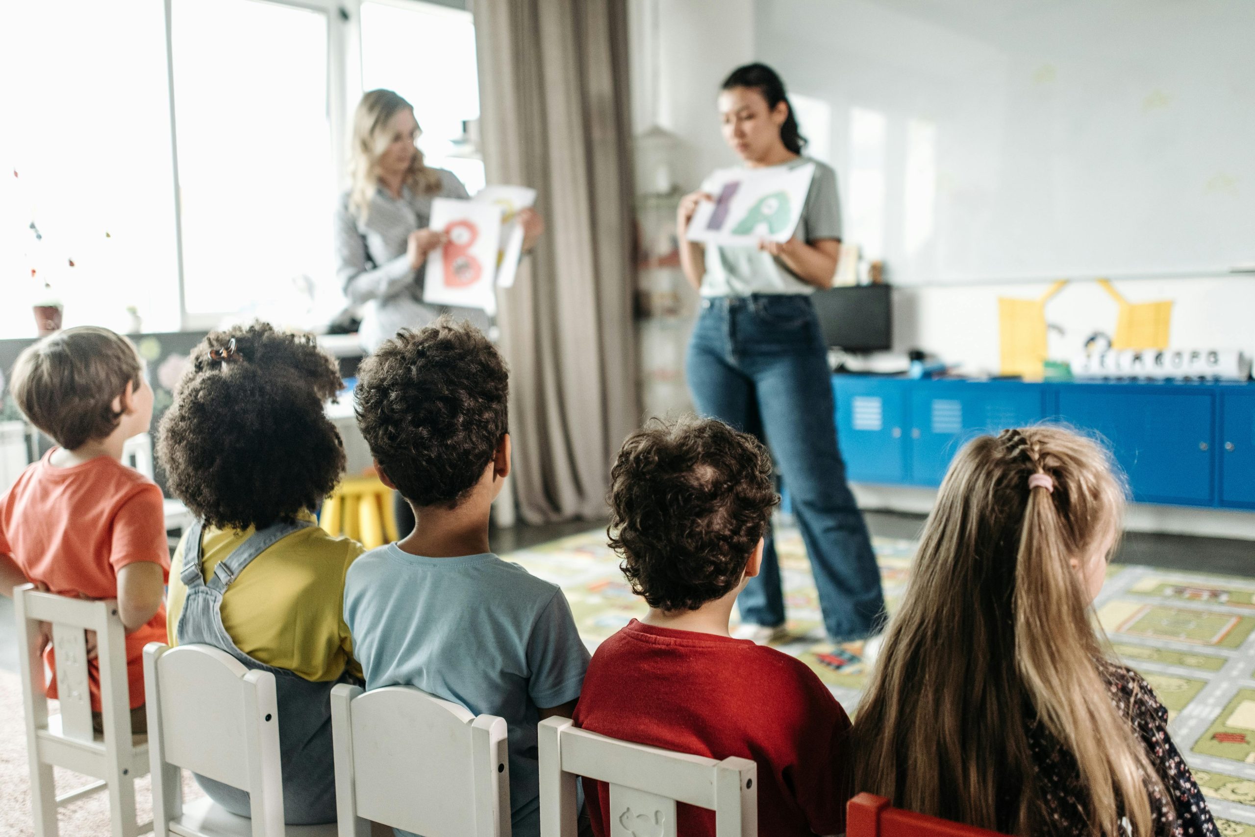 Niños sentados en sillas blancas dentro de un salón de clases