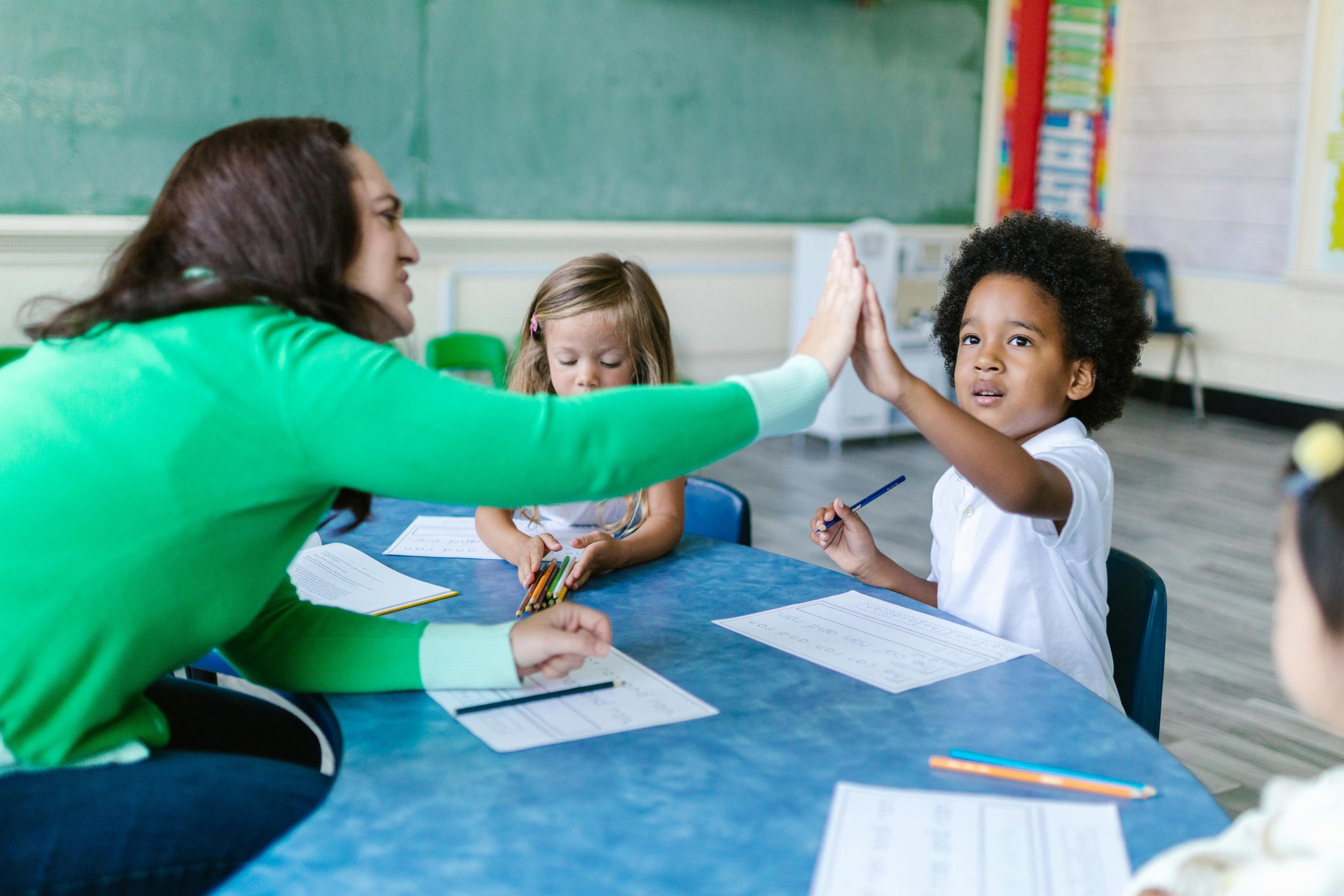 Maestra y niño dándose la mano en salón de clases.