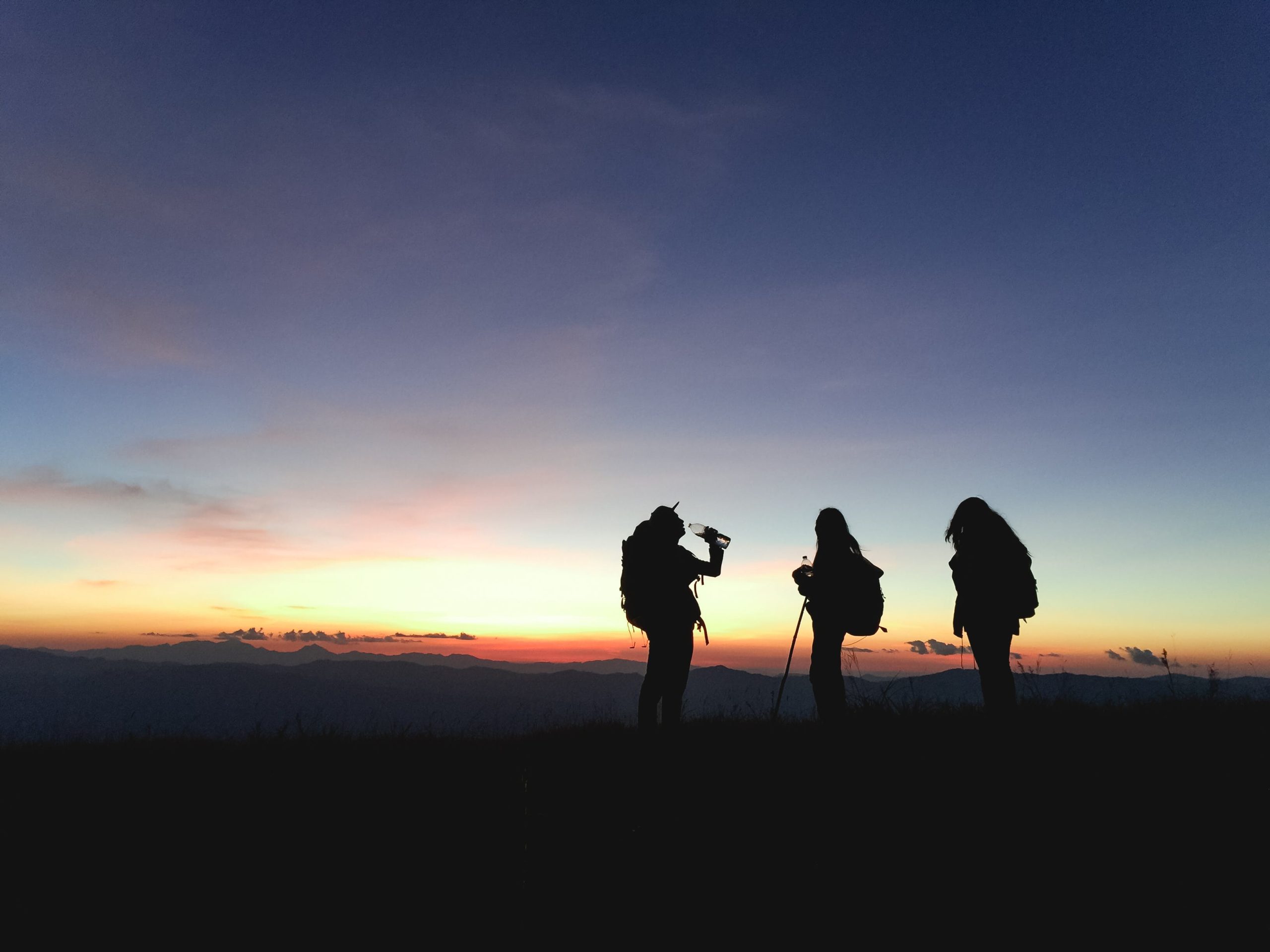 Tres senderistas admirando la vista de un atardecer.