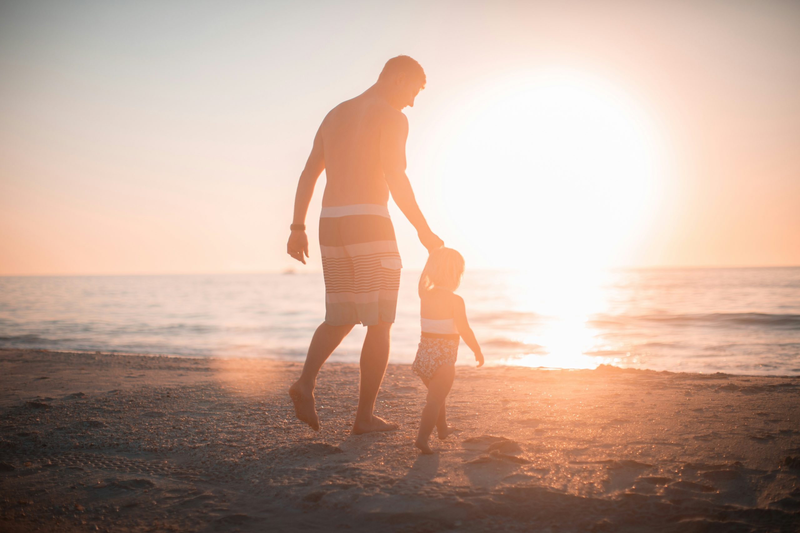 Padre tomando la mano de su hija mientras caminan en la playa.