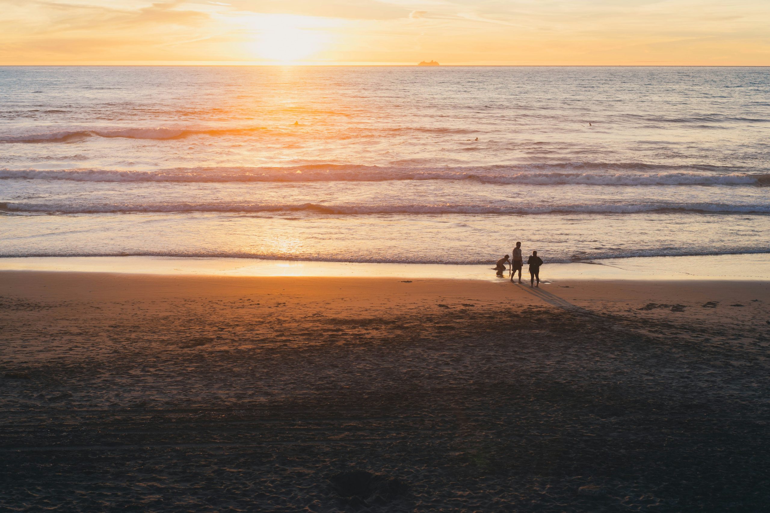 Familia de tres personas jugando a orillas de la playa durante un atardecer.