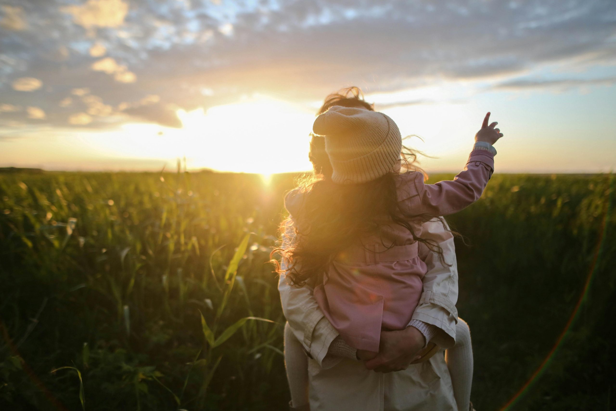 Madre cargando a su hija viendo el atardecer al aire libre.