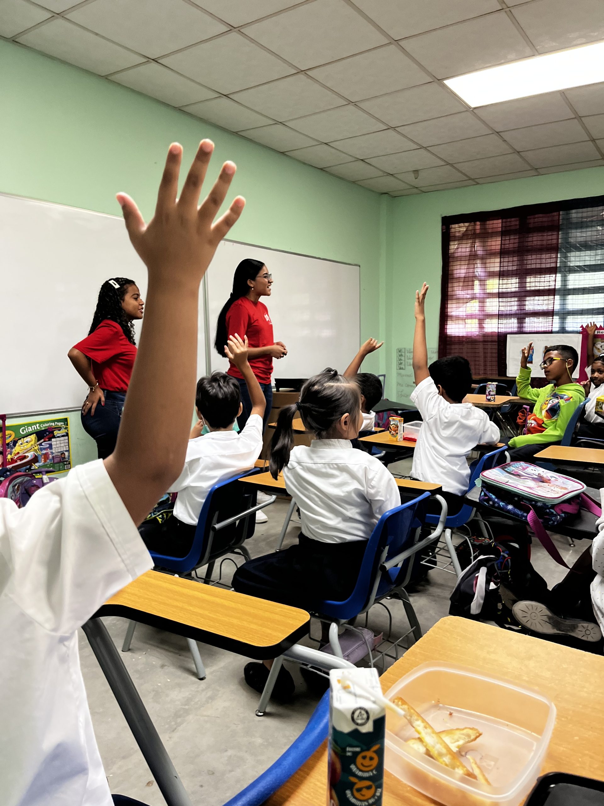 Dos voluntarias frente a una clase de estudiantes de escuela oficial.