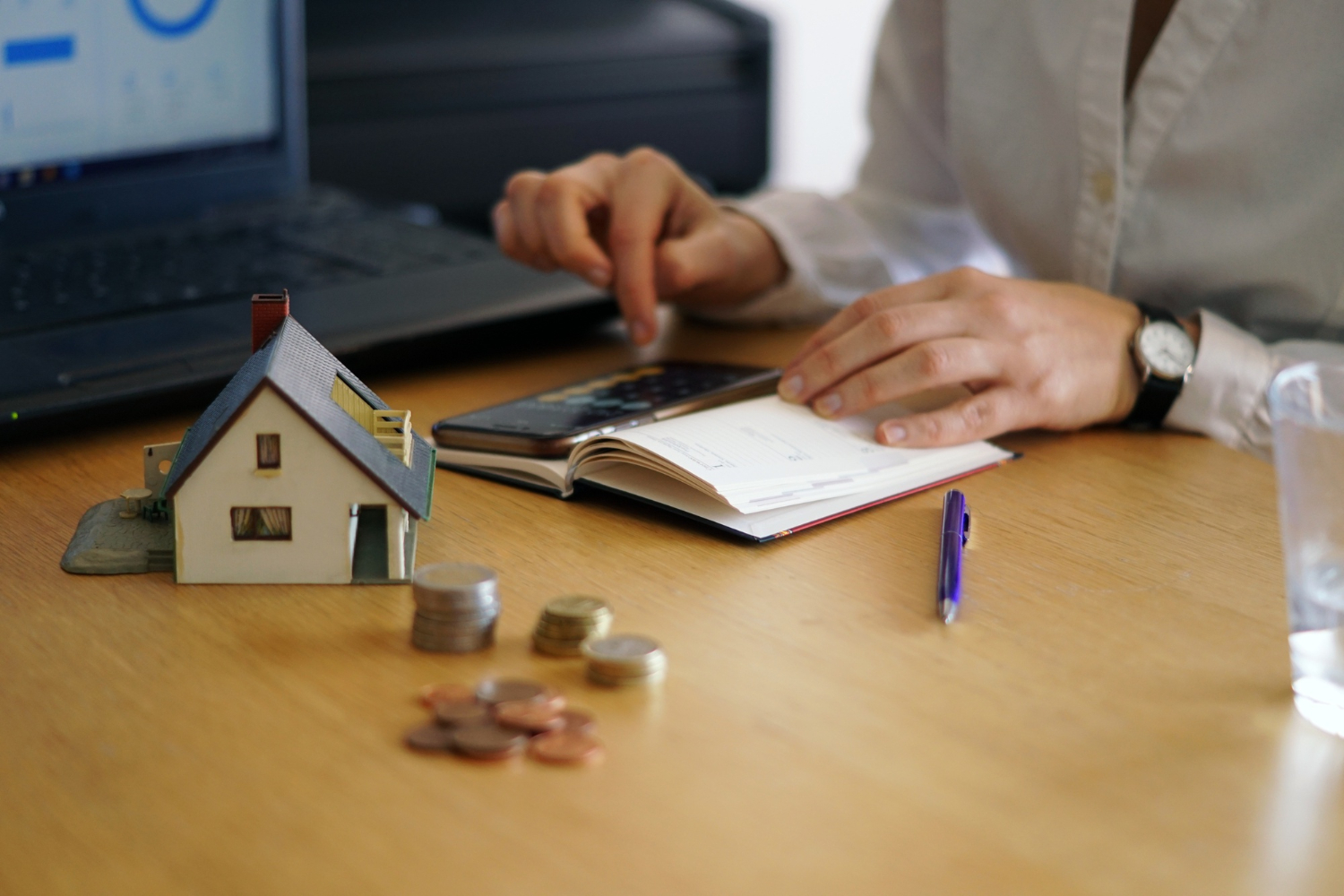 Persona calculando el Impuesto de Bienes Inmuebles en Panamá con calculadora y modelo de vivienda 