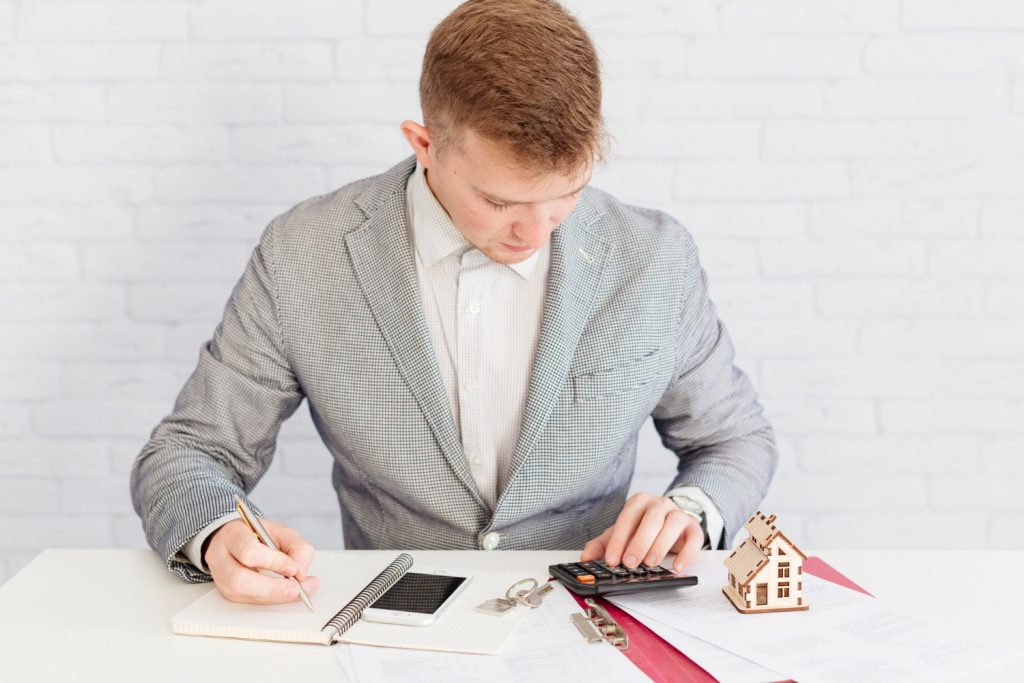 Persona revisando contrato de compraventa con calculadora y documentos, concepto de impuestos y cierre inmobiliario.