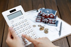 Persona con calculadora, documentos y maqueta de casa.